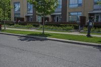 a couple of cars driving down a street next to a tall brown building on top of a lush green grass field