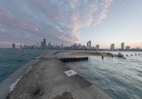 the concrete pier leads into a city skyline from the water's edge at sunset