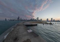 the concrete pier leads into a city skyline from the water's edge at sunset