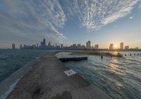 the concrete pier leads into a city skyline from the water's edge at sunset