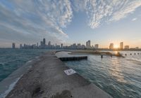 the concrete pier leads into a city skyline from the water's edge at sunset