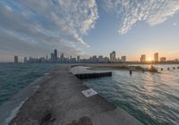 the concrete pier leads into a city skyline from the water's edge at sunset