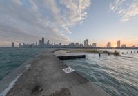 the concrete pier leads into a city skyline from the water's edge at sunset