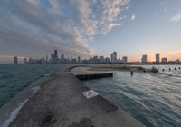 the concrete pier leads into a city skyline from the water's edge at sunset