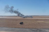 the airplane on the runway has black smoke rising from it's wings and tail