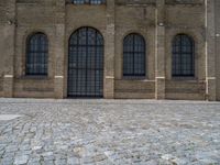 the sidewalk is paved with stones and has a bench in front of it, with no people inside