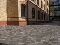 a sidewalk with chairs next to the brick building on the side, some have stairs and some buildings in the background