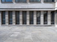 the corner of a concrete building next to glass windows with no one sitting outside and the building is made of blocks