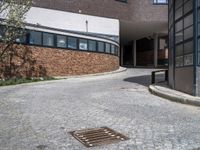 an urban brick building and a manhole with a concrete grill grate on the sidewalk