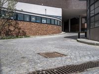 an urban brick building and a manhole with a concrete grill grate on the sidewalk