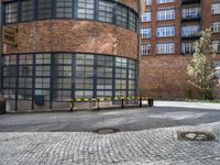 a paved brick and metal walkway with yellow barriers and trees growing inside a large building