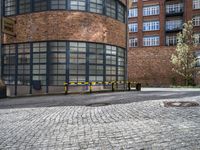 a paved brick and metal walkway with yellow barriers and trees growing inside a large building