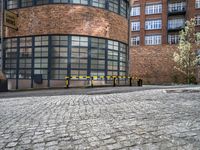 a paved brick and metal walkway with yellow barriers and trees growing inside a large building