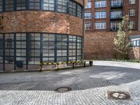 a paved brick and metal walkway with yellow barriers and trees growing inside a large building