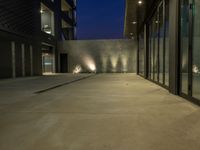 a courtyard in the evening with two wall lamps and a building behind it that has windows