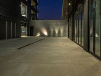 a courtyard in the evening with two wall lamps and a building behind it that has windows