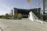 an urban courtyard with various benches and trees near a building under a clear sky with some buildings in the background