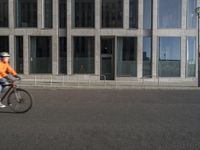 the person rides his bike on the street near a tall building with large windows and glass windows