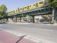 a woman riding her bicycle on the side of a road while a pedestrian crosses a bridge over the street