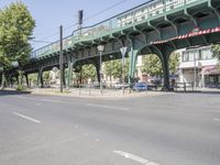 a woman riding her bicycle on the side of a road while a pedestrian crosses a bridge over the street