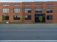 an empty street in front of a large red brick building on the other side of the road is a street light that has a line for motorists