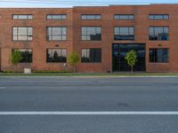 an empty street in front of a large red brick building on the other side of the road is a street light that has a line for motorists