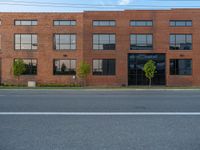 an empty street in front of a large red brick building on the other side of the road is a street light that has a line for motorists