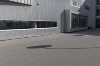 the young man skateboards on the paved parking space outside a large building on a sunny day