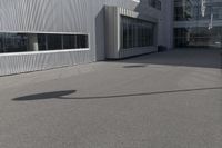 the young man skateboards on the paved parking space outside a large building on a sunny day