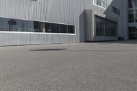 the young man skateboards on the paved parking space outside a large building on a sunny day