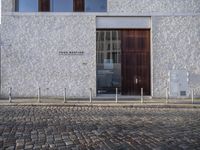 a cobblestone road in front of a large white building, with a wooden entrance and two doors