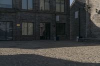 the person is walking down the street near old buildings on a sunny day with a red umbrella