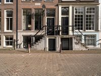 stairs and railings leading to three buildings on an empty sidewalk in the city of amsterdam, netherlands