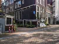 two tall brick buildings along a street with no parking spaces for cars and people outside