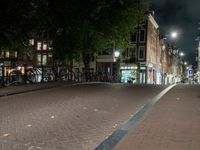 a city street with bikes and some lights in the distance next to buildings at night