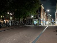 a city street with bikes and some lights in the distance next to buildings at night