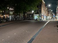 a city street with bikes and some lights in the distance next to buildings at night