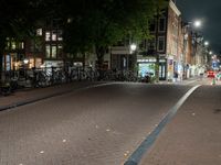 a city street with bikes and some lights in the distance next to buildings at night