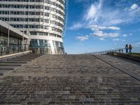 a walkway up to the top of a building on the beach with people and buildings in the background