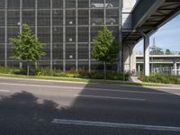 the side of a tall building next to a street with lots of trees and flowers