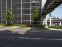 the side of a tall building next to a street with lots of trees and flowers