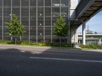 the side of a tall building next to a street with lots of trees and flowers