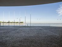 a man with a surfboard is walking on a pavement near the water and other poles