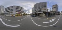 a city with buildings in the background as seen from a fish eye lens, and blue car on the side