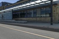 a long paved sidewalk next to an urban building and road with glass doored windows