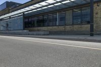 a long paved sidewalk next to an urban building and road with glass doored windows