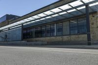 a long paved sidewalk next to an urban building and road with glass doored windows