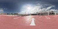 a 360 - angle view of a curved airport runway with the clouds overhead and buildings in the foreground