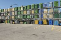 stacks of large containers are on a large racked area by a fence and street light