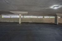 there is a empty parking garage with no cars parked on the pavement in it, and an empty parking area at one end